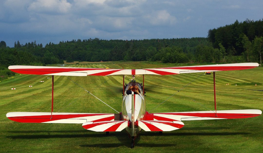 A biplane with red and white stripped wings about to take off on a grass airstrip